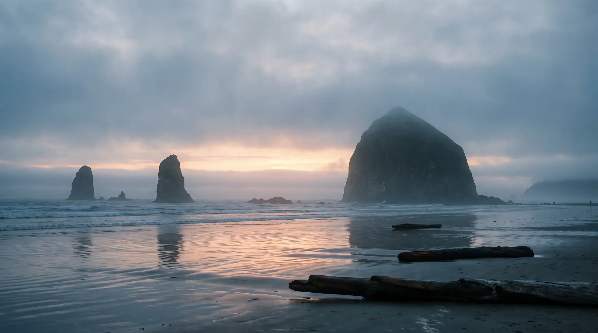 Sea stacks on the Washington coast silhouetted in layered fog as the first pale light breaks over the water